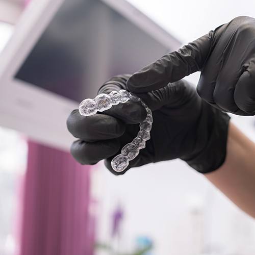 Dentist with black gloves pointing to clear aligner