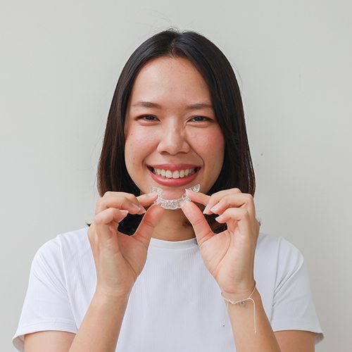 Woman smiling while holding clear aligner